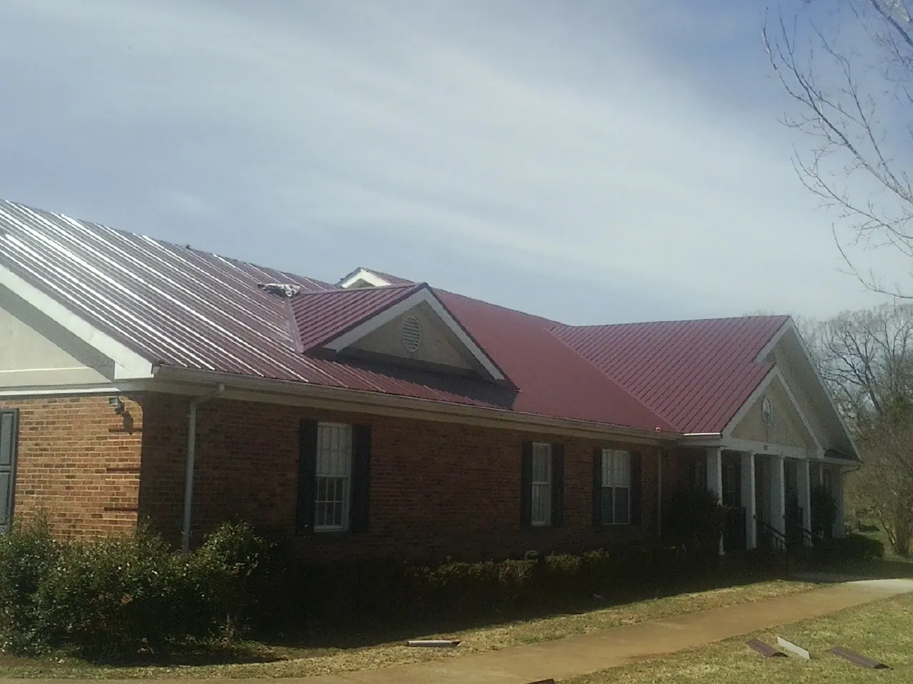 Red metal roof with gabled entries on a long brick building, from a Hail Damage Roof Repair job in Deersville