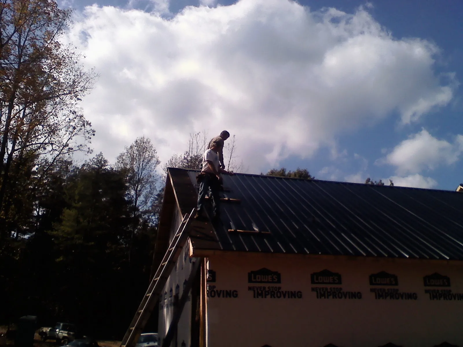 Roofer fastening dark metal panels high against a cloudy sky, from a Roof Inspection job in Deersville