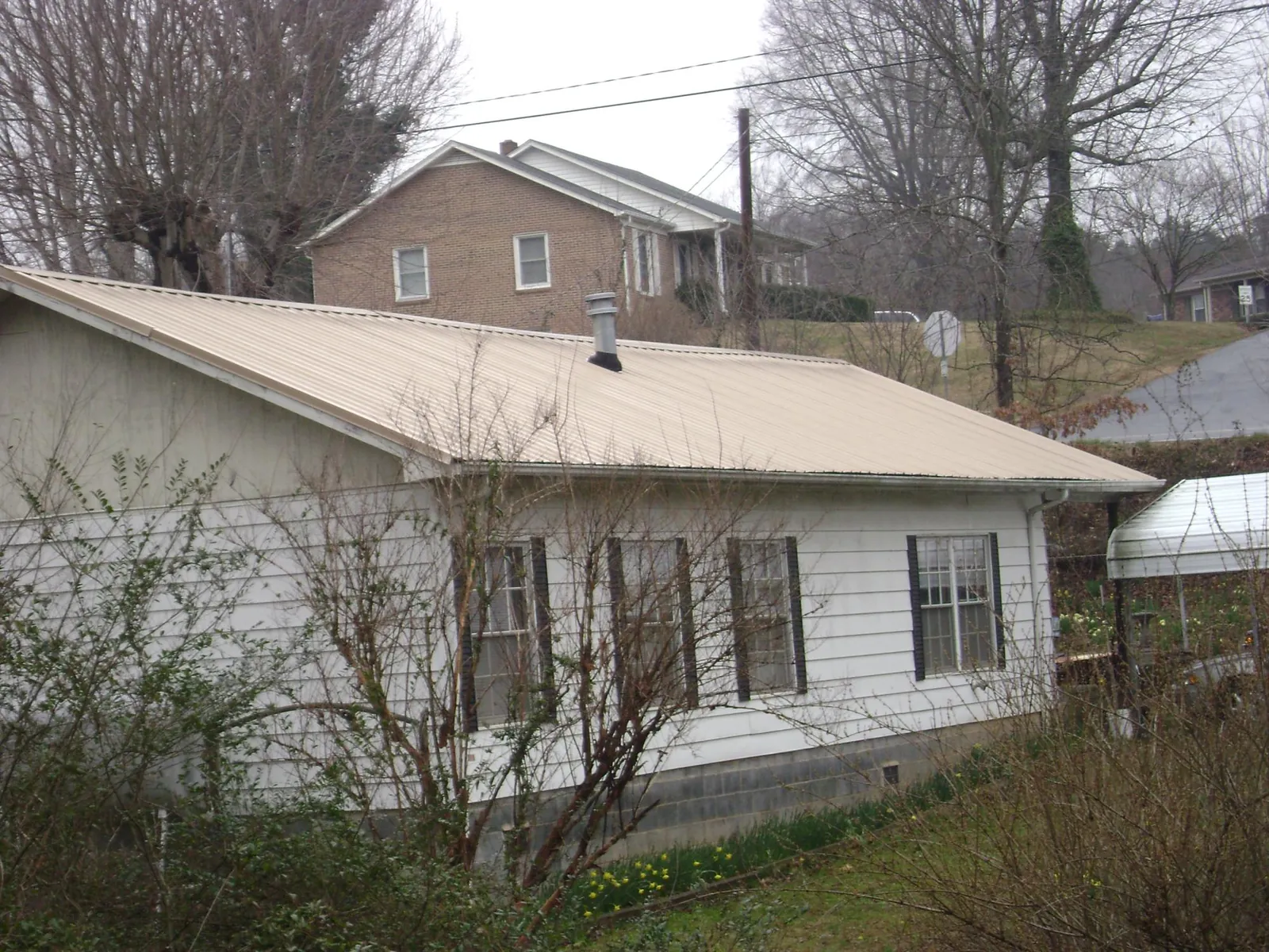 Tan metal roof on a white sided house set into a hillside — Commercial Roofing by Roofing Brothers in Deersville
